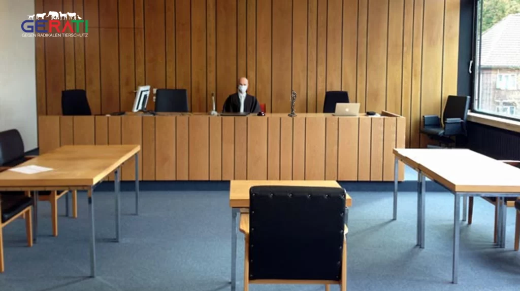 Ein Bild eines Gerichtssaals in Deutschland, in dem die Privatsphäre eines Angeklagten verletzt wird. Es zeigt einen Richter, eine überfüllte Zuschauertribüne und einen verängstigten Angeklagten, wobei das Ungleichgewicht der Macht und die Ungerechtigkeit des Prozesses betont werden.