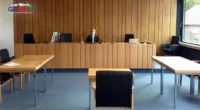 Ein Bild eines Gerichtssaals in Deutschland, in dem die Privatsphäre eines Angeklagten verletzt wird. Es zeigt einen Richter, eine überfüllte Zuschauertribüne und einen verängstigten Angeklagten, wobei das Ungleichgewicht der Macht und die Ungerechtigkeit des Prozesses betont werden.