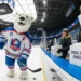 Ein Eisbär in Eishockey-Ausrüstung der Berliner Eisbären steht in einem Stadion neben Fans, die Spenden für das Tierheim sammeln – Darstellung der Partnerschaft Eisbären Berlin Tierheim.