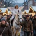 Weißes Pferd mit Engelreiterin wird dicht an dicht durch einen beleuchteten Weihnachtsmarkt geführt während umstehende Besucher kritisch beobachten und so den umstrittenen Pferdeinsatz Weihnachtsmarkt zeigen