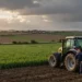 Umweltschutz Landwirtschaft Anreize – Agrarpolitik zwischen Anspruch und Wirklichkeit 3 Landwirt steht bei Sonnenaufgang auf einem europäischen Feld mit Traktor, Windrädern und Blühstreifen als Symbol für Umweltschutz Landwirtschaft Anreize