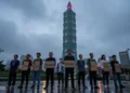 PETA - Alex Honnold und die Inszenierung veganer Leistungsfähigkeit 47 Aktivisten stehen mit leeren Schildern vor dem beleuchteten Taipei 101 bei Regen, während hoch oben ein Kletterer zu sehen ist und die Szene die umstrittene Aktion PETA Alex Honnold symbolisiert