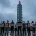 PETA - Alex Honnold und die Inszenierung veganer Leistungsfähigkeit 6 Aktivisten stehen mit leeren Schildern vor dem beleuchteten Taipei 101 bei Regen, während hoch oben ein Kletterer zu sehen ist und die Szene die umstrittene Aktion PETA Alex Honnold symbolisiert