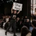 Protestaktion während einer Modenschau: Eine Aktivistin hält ein „Stop Mohair“-Plakat hoch. Das Titelbild zum Thema PETA Paul Smith Mohair zeigt die Debatte zwischen Tierrechtsaktivismus und Modeindustrie.