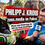 Philipp J. Kroiß von zoos.media und GERATI-Herausgeber Silvio Harnos vor einer Zoo-Kulisse mit Tieren und Anti-Zoo-Protestschildern.